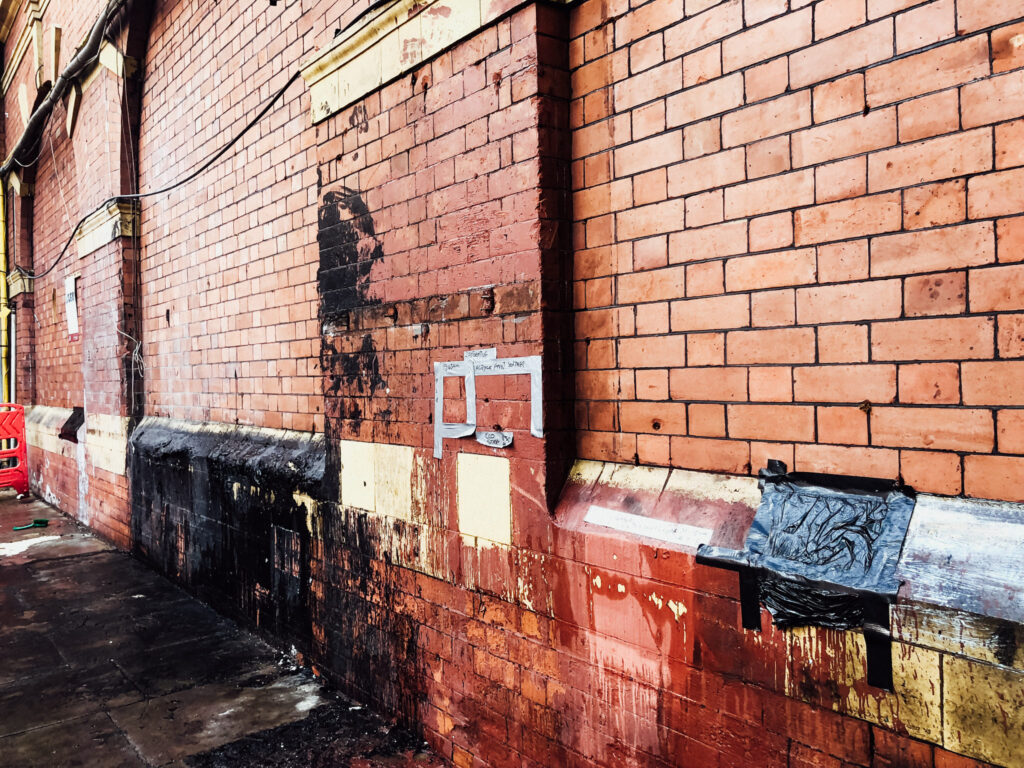 Old brick and stone facade with different looking patches across, some cleaner than others