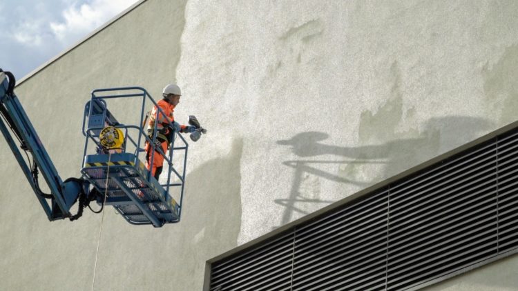 Man in cradle respraying rendered building