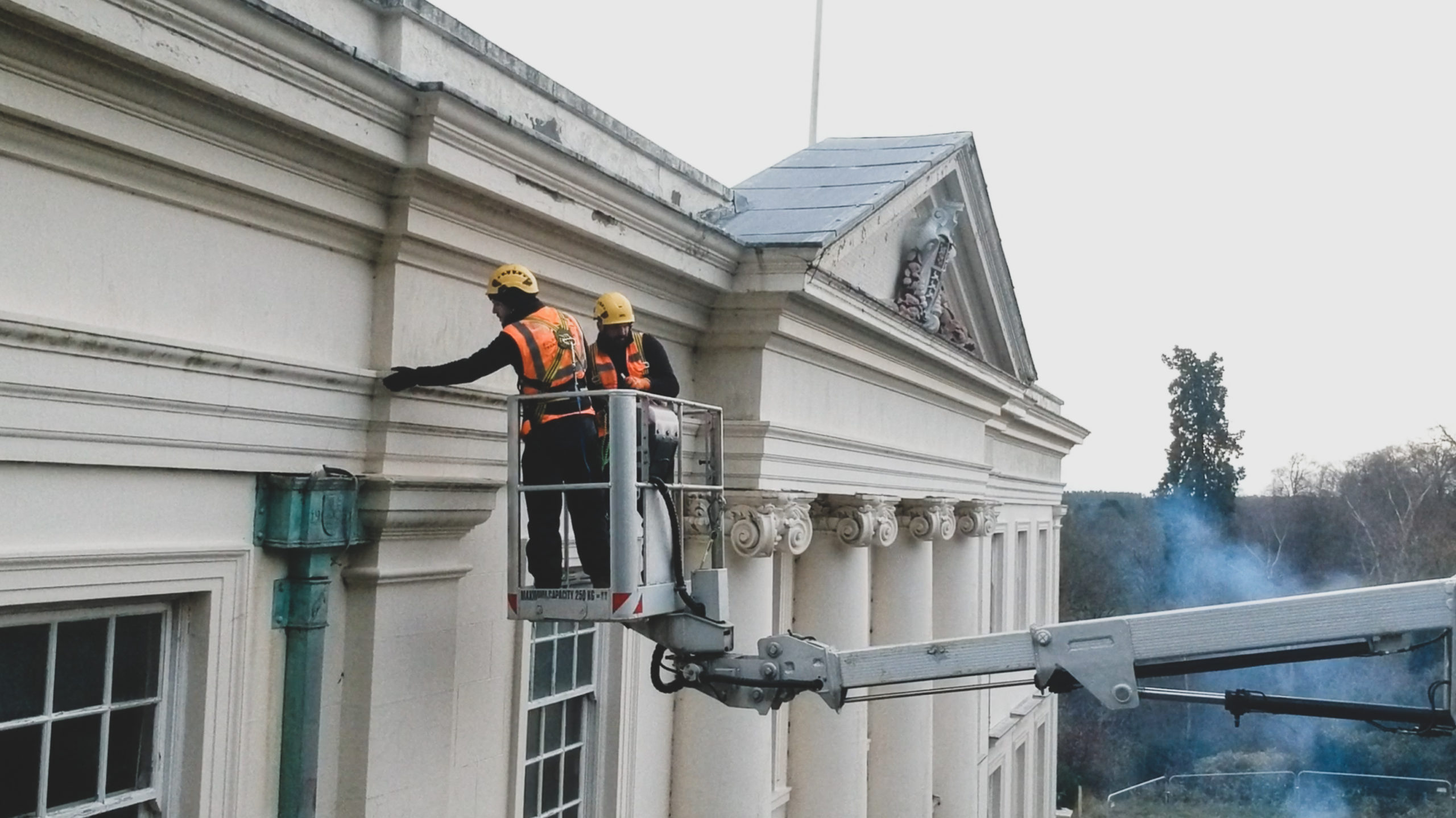 Listed cream rendered building being surveyed by two workers via MEWP access