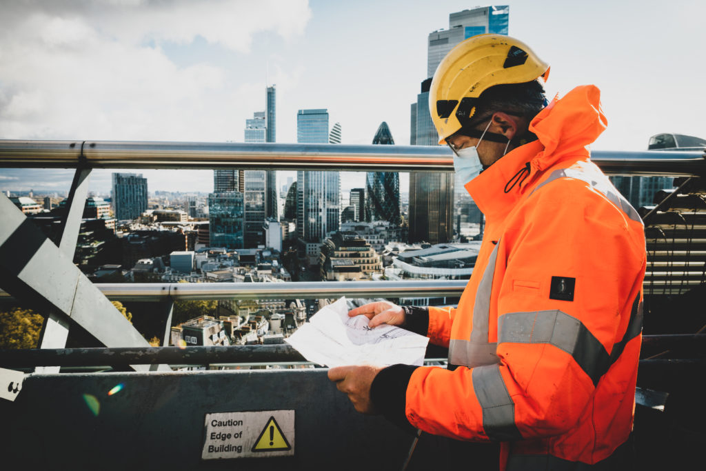 person in high vis safety gear reading a document on top of a building in london