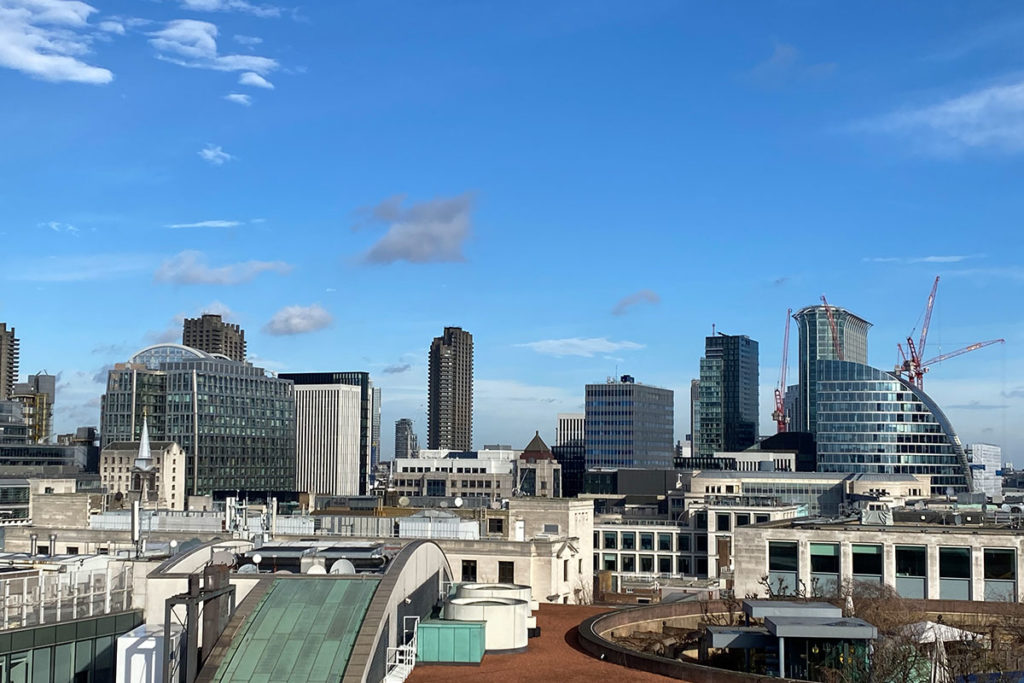 London city skyline with modern skyscrapers under a bright blue sky, featuring cranes in the distance.