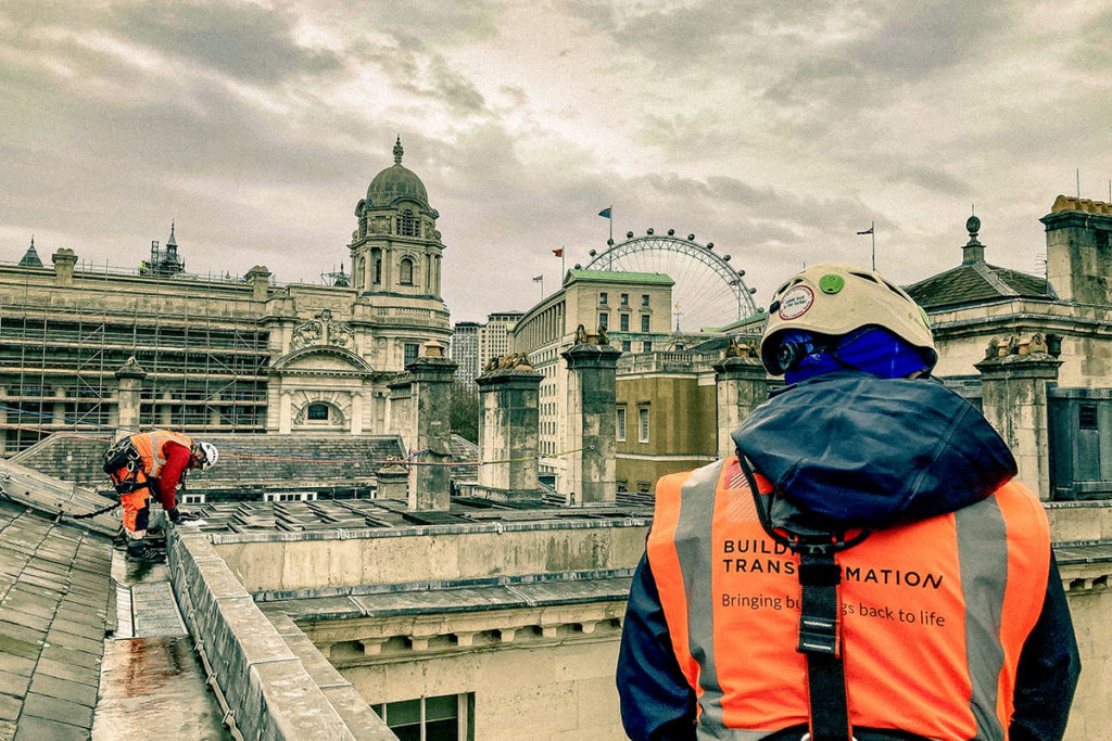 Construction workers in safety gear on London rooftop, with London Eye in background, Building Transformation.