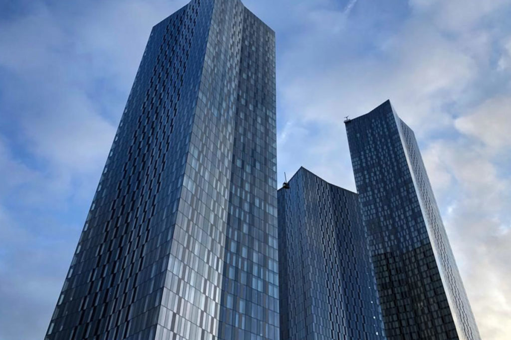 Modern, reflective skyscrapers with glass facades against a cloudy blue sky in an urban skyline.