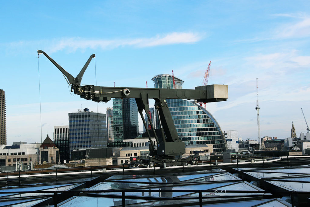 Rooftop cranes set against a cityscape of modern skyscrapers and clear blue sky. Urban development scene.