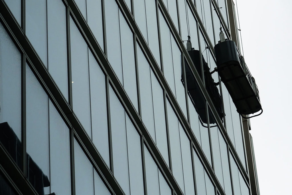 Window cleaning platform suspended on modern glass skyscraper with sleek facade reflection.