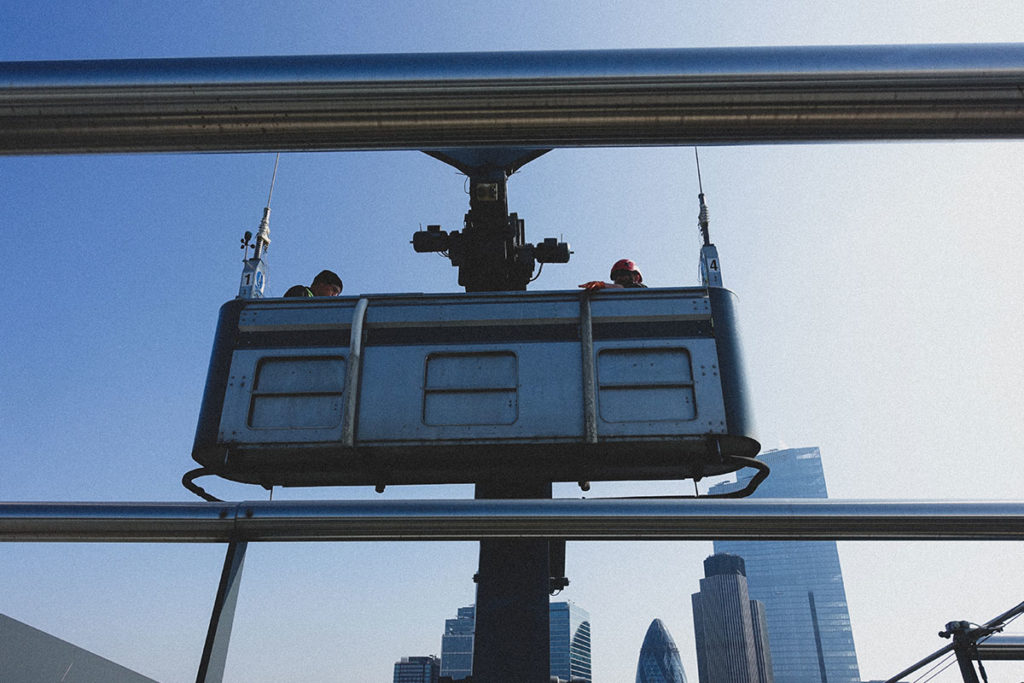 Window cleaners in a suspended cradle high above London's skyline, with iconic skyscrapers in view.