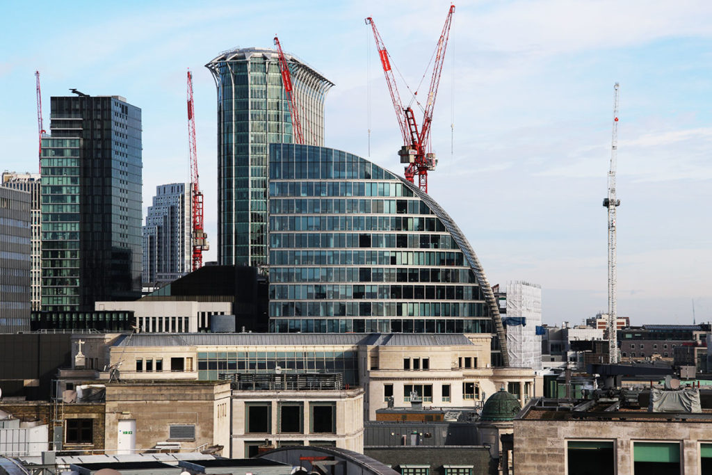 Modern London skyline with curved glass building and red cranes against a clear blue sky.