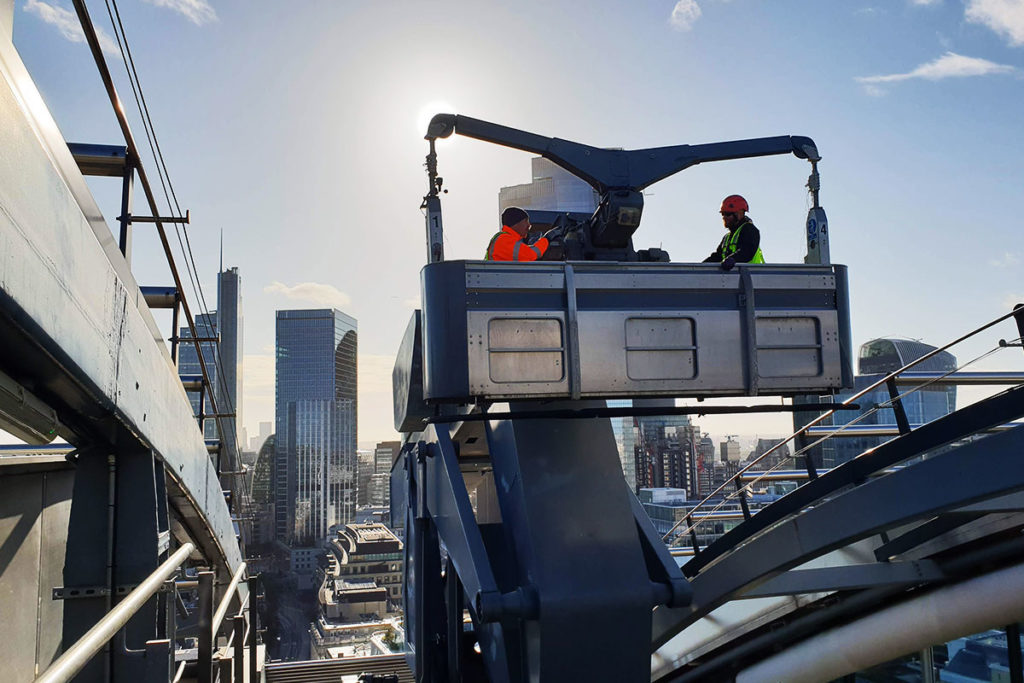 Workers in lift basket against city skyline, sun shining behind skyscrapers, construction scene.