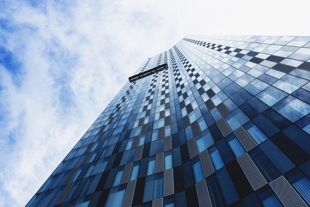 Modern skyscraper with reflective blue glass facade extending into a bright, cloudy sky.
