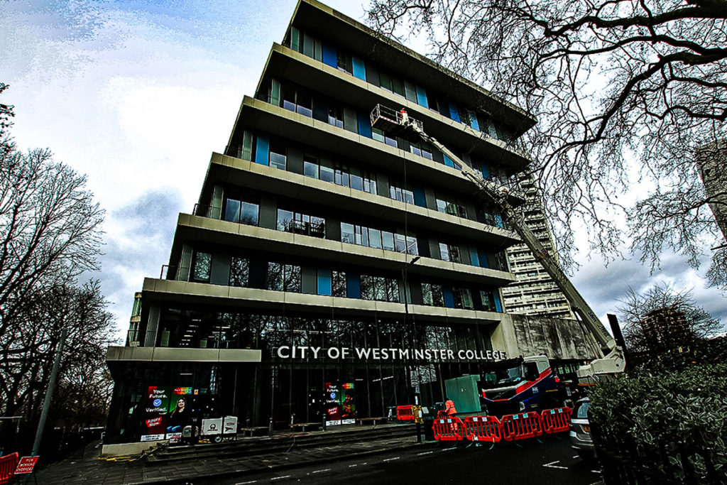 City of Westminster College modern building, asymmetrical architecture, crane lift, surrounded by trees.