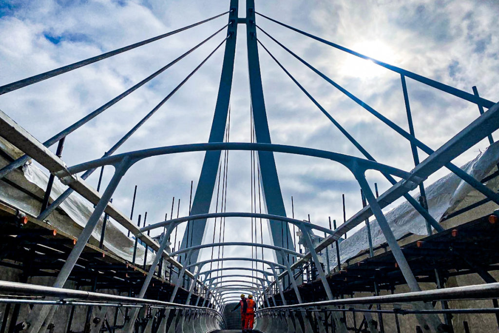 Dramatic view of construction site with two workers beneath towering metal structure against a cloudy sky.