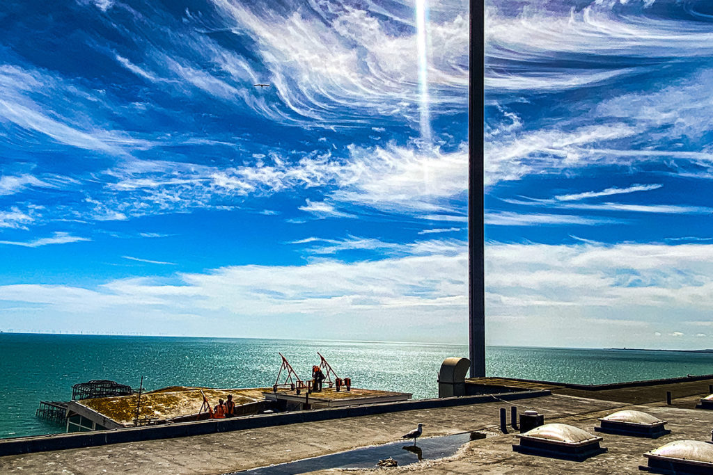 Vibrant blue sky with swirling clouds over a serene sea, rooftop view with a solitary seagull.