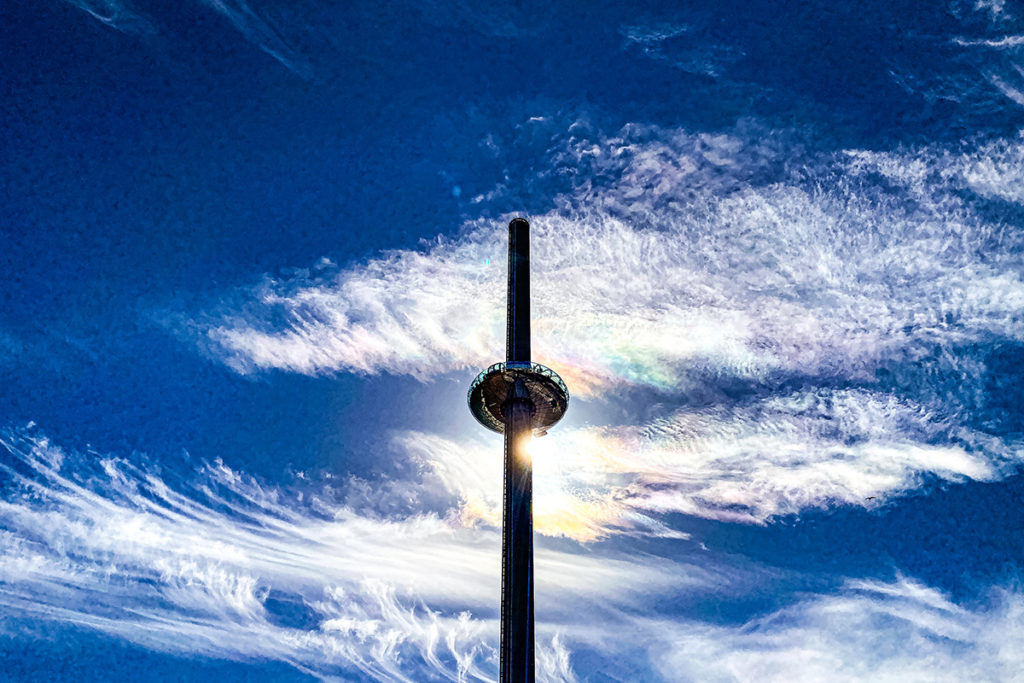 Brighton's i360 tower silhouetted against a vivid blue sky with swirling white clouds.