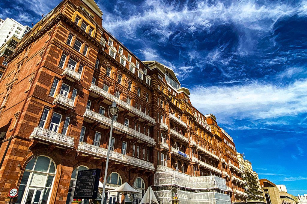 Historic red-brick hotel with white balconies under vibrant blue sky, Brighton, UK.