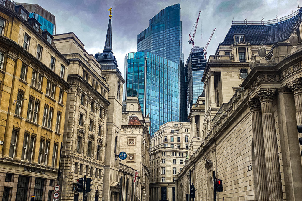 Historic and modern architecture in London, featuring columns and glass skyscrapers under a cloudy sky.
