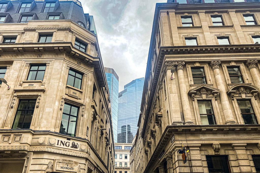 Historical London buildings on Moorgate, flanked by modern glass skyscrapers under a cloudy sky.