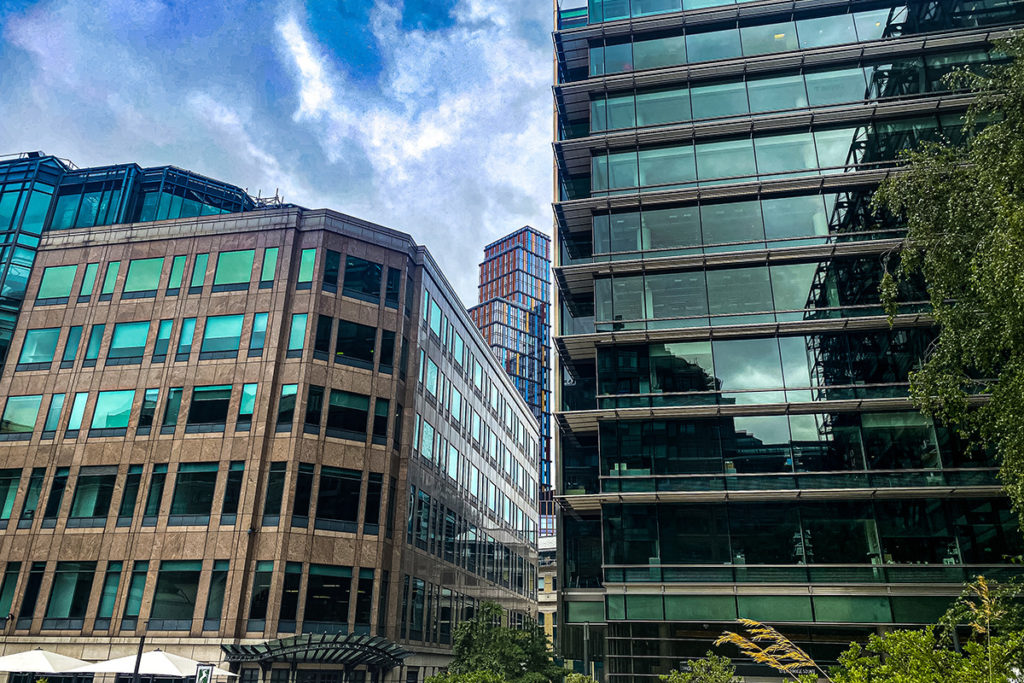 Modern office buildings with reflective glass facades under a partly cloudy sky, surrounded by greenery.