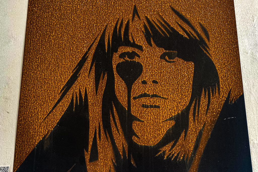 Rust-coloured stencil art depicting a woman's face with textured hair on a rough surface.