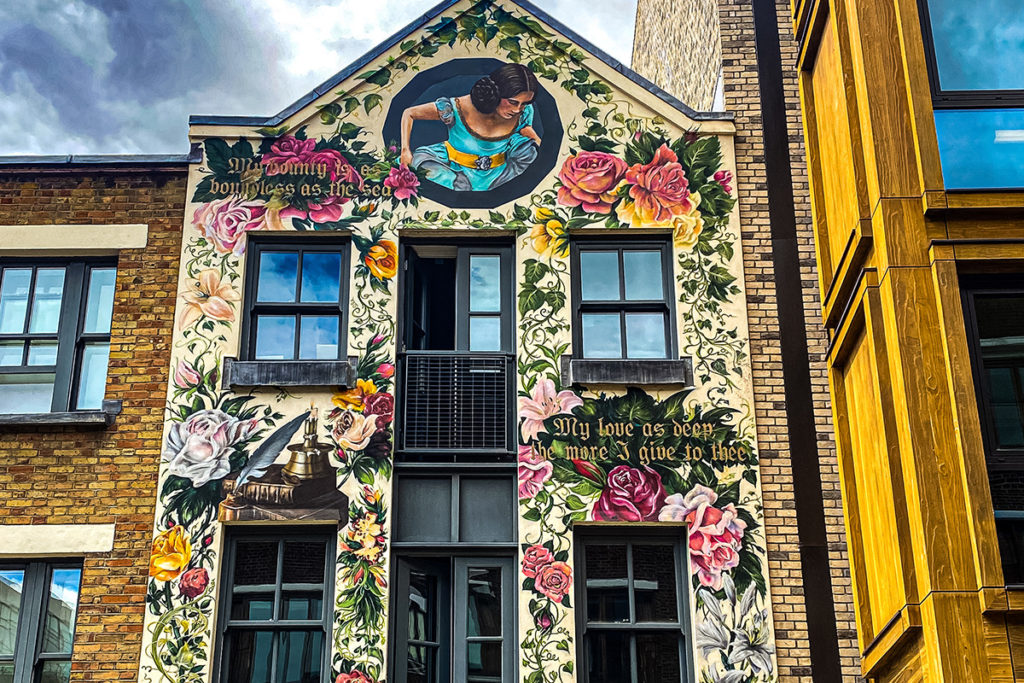 Historic building mural with vibrant floral design. Text reads, My bounty is as boundless as the sea.