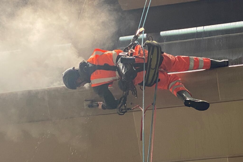 Worker in orange safety gear and helmet abseiling on a foggy construction site, performing maintenance.