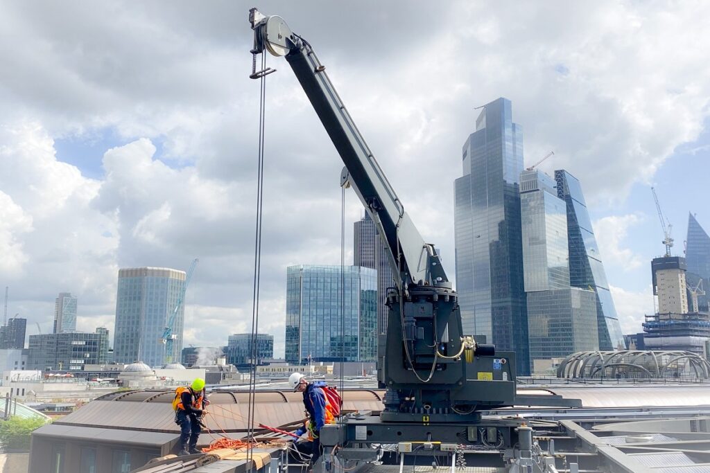Construction workers on rooftop with crane against a backdrop of modern skyscrapers and cloudy sky.