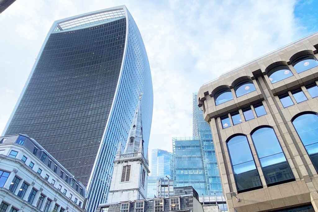 Modern skyscrapers and historic church steeple under bright blue sky in London's financial district.