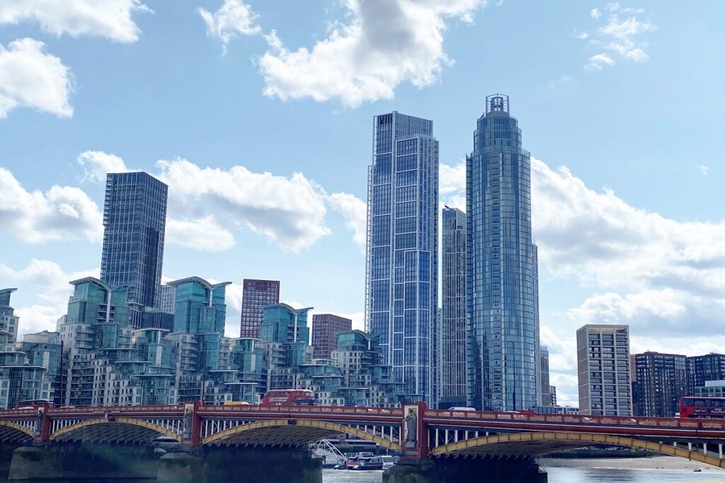 Modern London skyline with towering skyscrapers and red double-decker buses crossing Vauxhall Bridge.