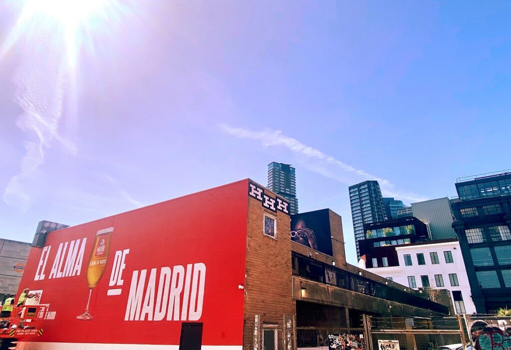 Sunny day over an urban mural with EL ALMA DE MADRID on a red wall, skyscrapers in the background.