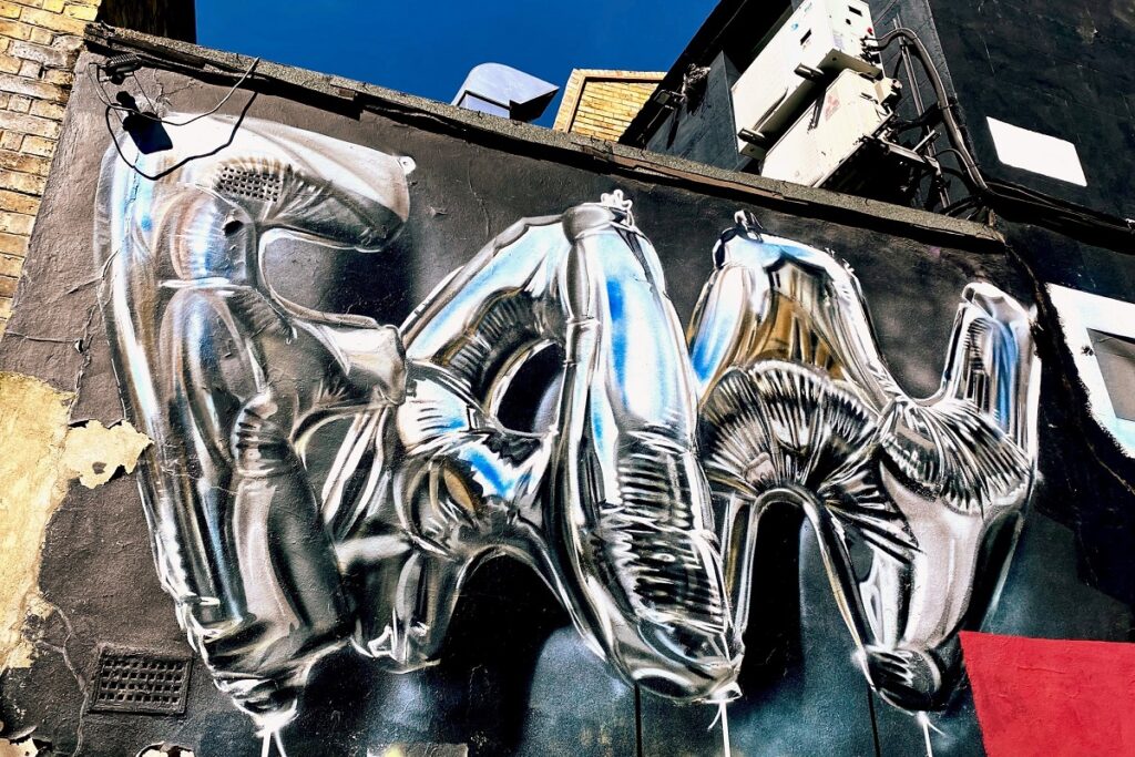 Chrome balloon graffiti spelling RAW on an urban wall, contrasting with a vibrant blue sky.
