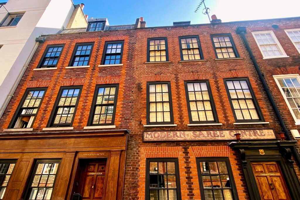 Historic red brick building with black-framed windows, sign reading MODERN SAREE CENTRE, under clear sky.