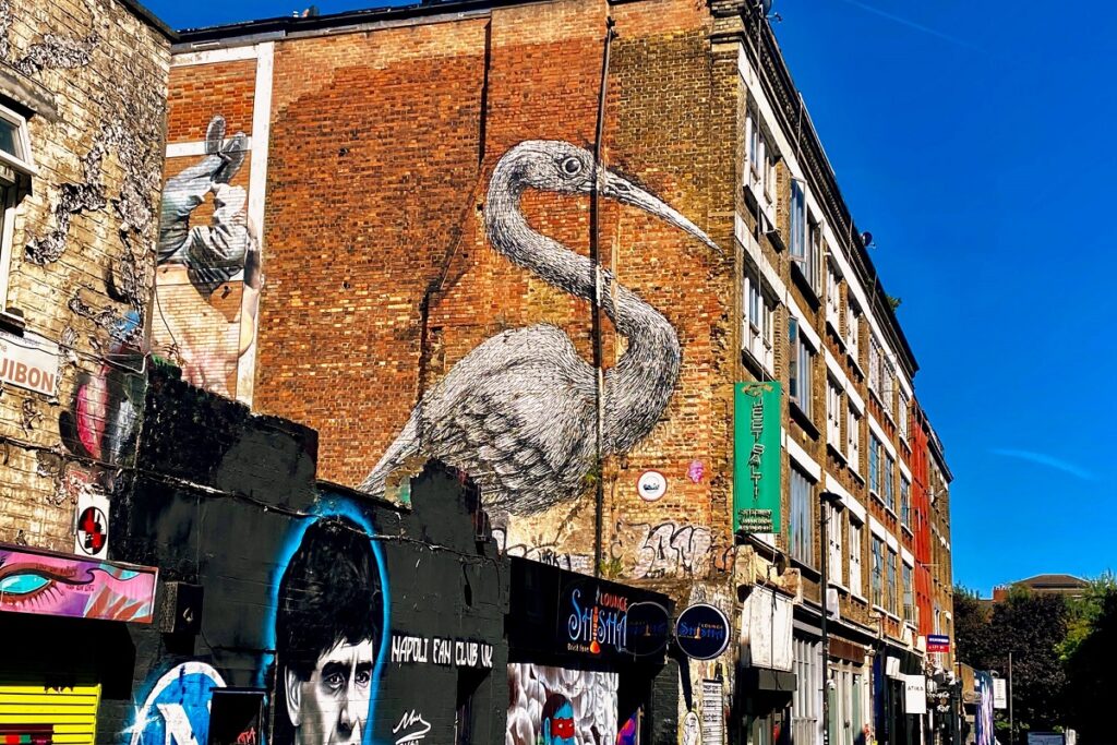 Street art of a large heron on a red brick wall in Shoreditch, with vibrant murals and bright blue sky.