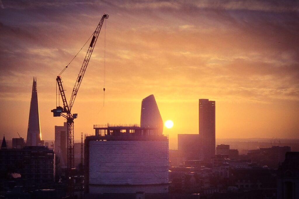 Cranes and skyscrapers silhouetted against a golden London sunset, with the Shard prominent.