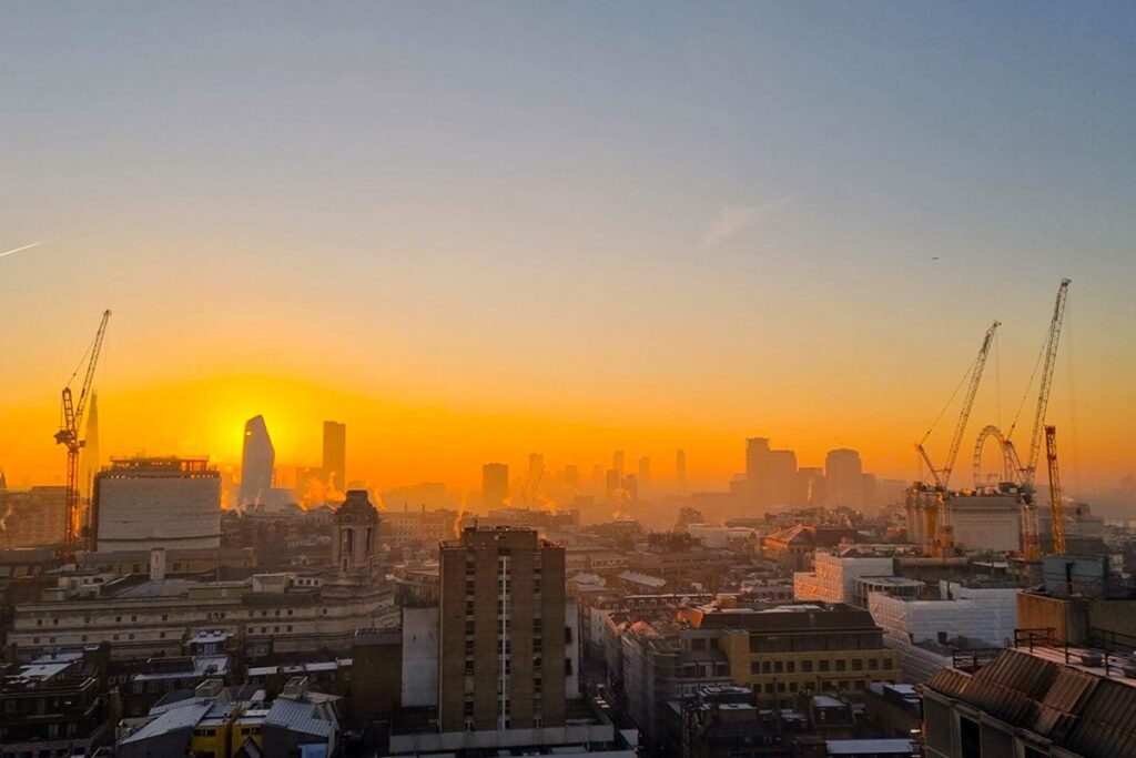 Sunrise over London skyline with cranes, urban landscape, and glowing orange sky.