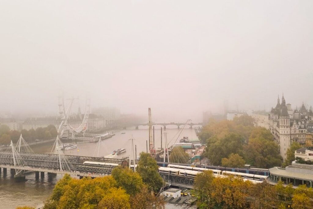 Foggy view of London with the London Eye, River Thames, and Victorian architecture, shrouded in mist.