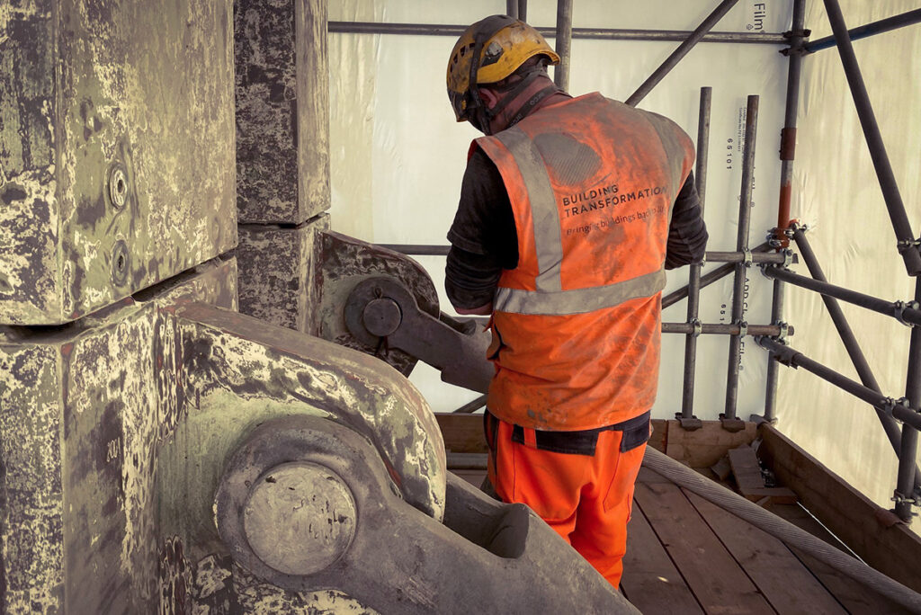 Construction worker in orange vest, marked Building Transformation, operates machinery on scaffolding.