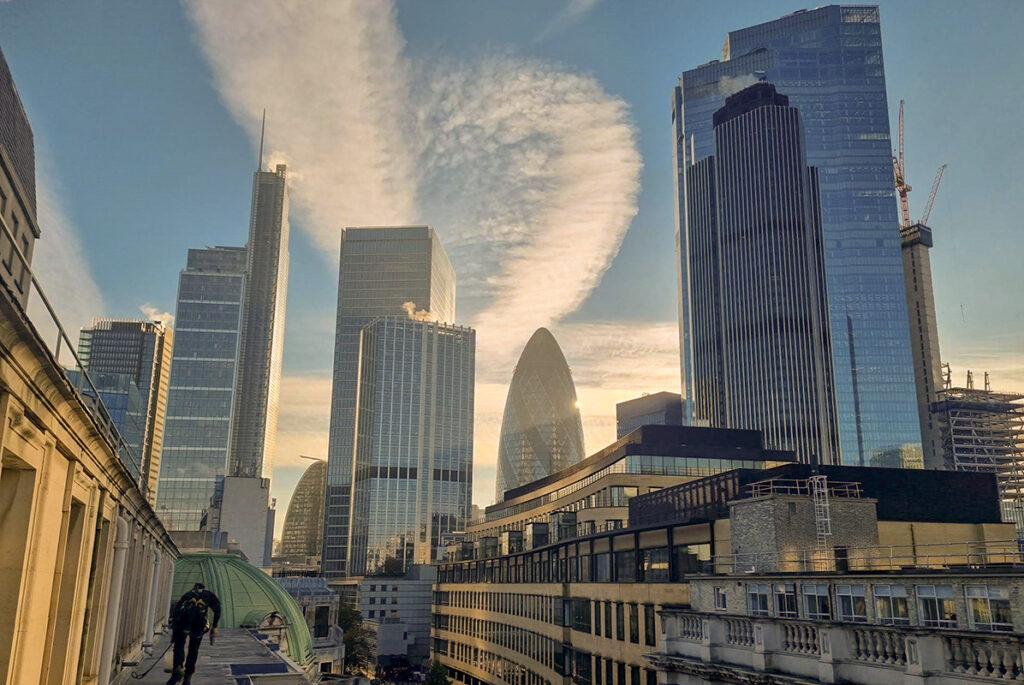 London skyline at sunset, featuring iconic skyscrapers like the Gherkin under a dramatic sky.