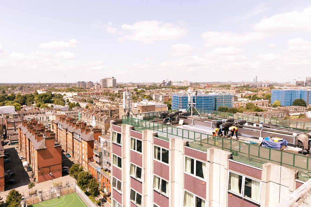 Cityscape with workers on a rooftop, modern buildings in distance, under a sky filled with fluffy clouds.