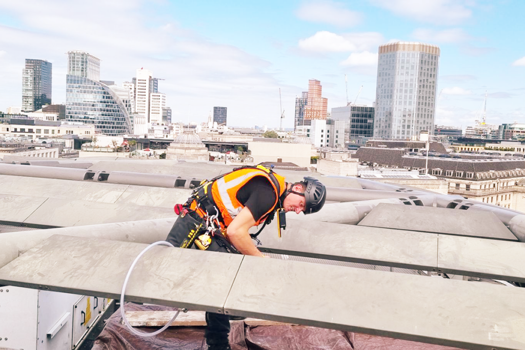 Construction worker in safety gear inspects rooftop in cityscape with modern high-rise buildings.