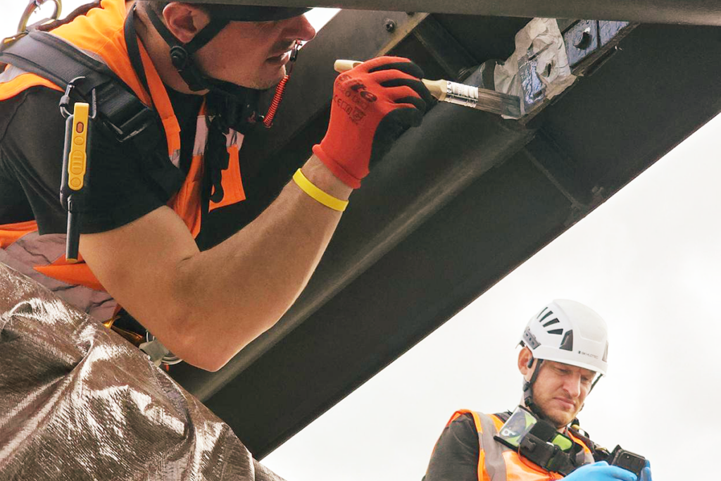 Construction workers in safety gear painting steel beams on a bridge with care and precision.
