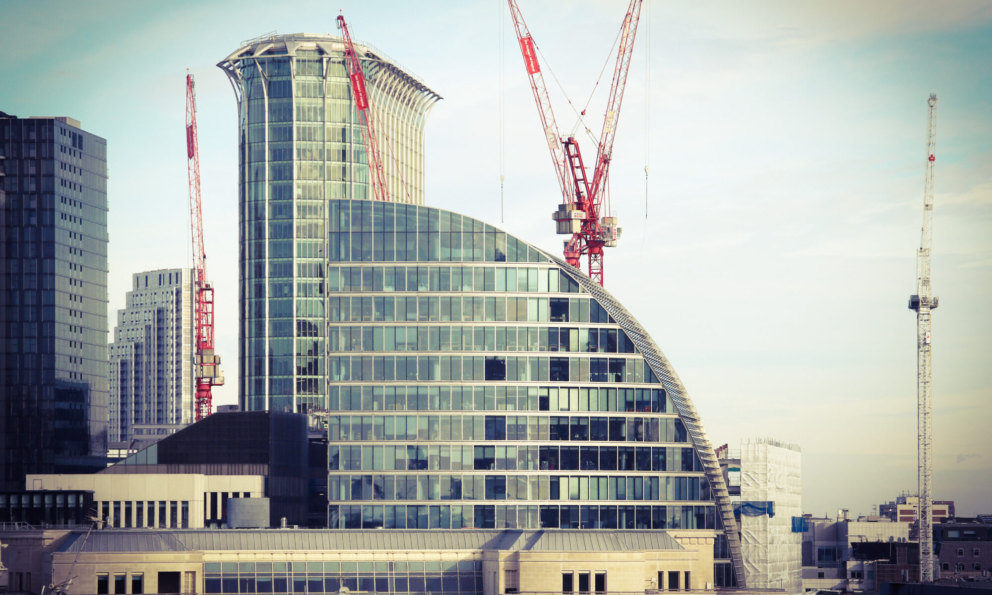 Modern skyline with glass buildings and red construction cranes against a pale sky, creating an urban scene.