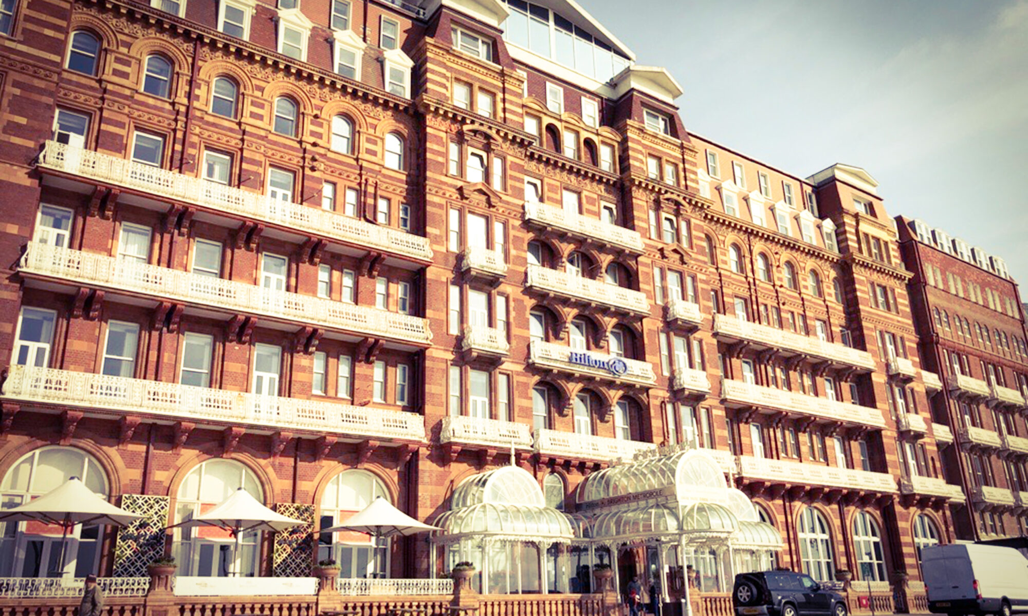Historic Hilton hotel in sunlit, ornate red-brick building with white balconies and entrance canopy.