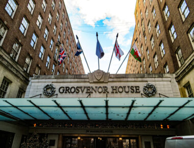 Grand entrance of Grosvenor House with festive wreaths, flags, and JW Marriott Hotel signage under blue sky.