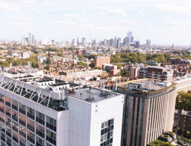 Aerial view of London skyline with modern skyscrapers and historic buildings, under a clear blue sky.